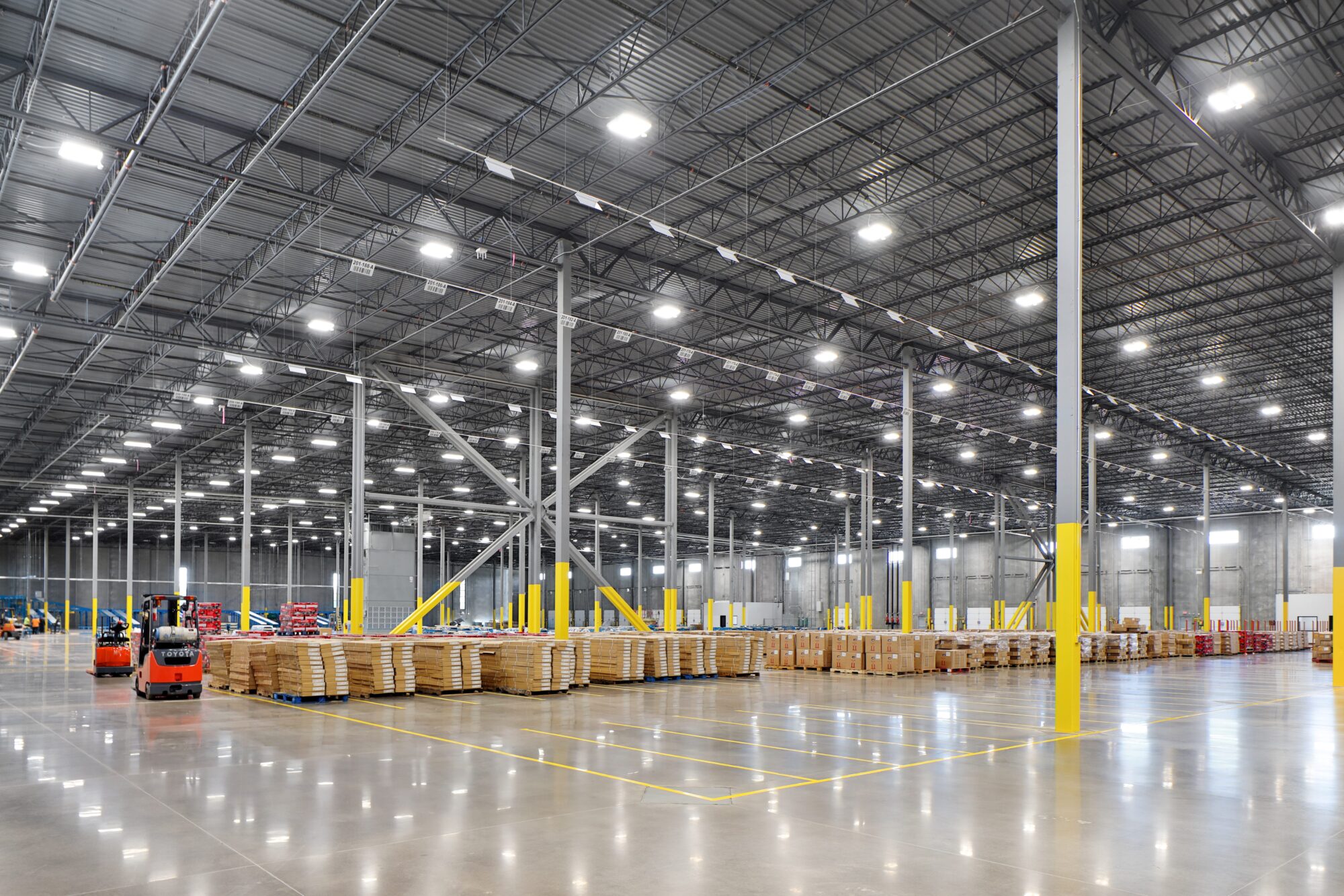 Interior of large warehouse industrial building with parked forklifts, shipping containers, and crates