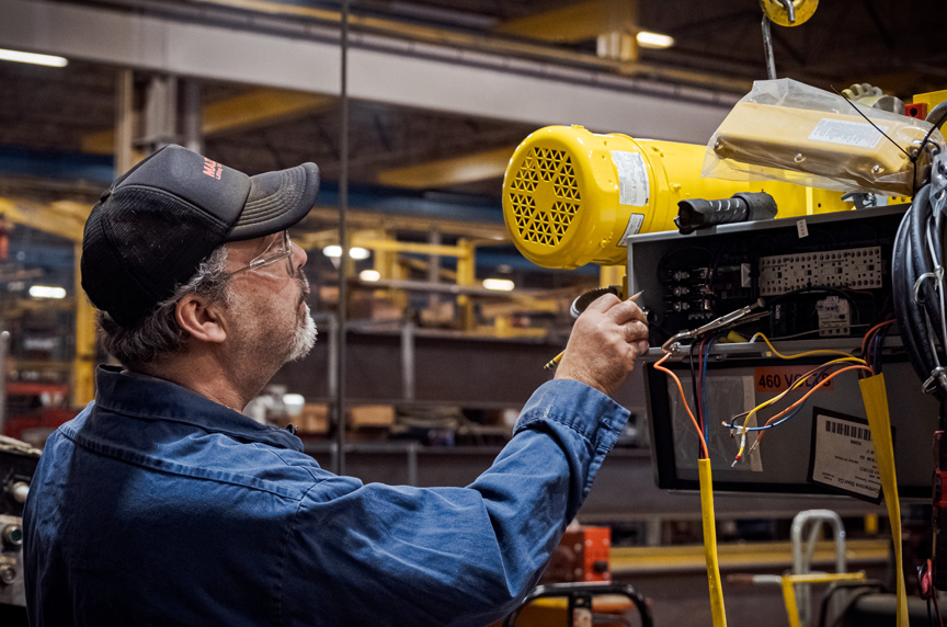 Crane hoist technician inspects electrical panel on hoist