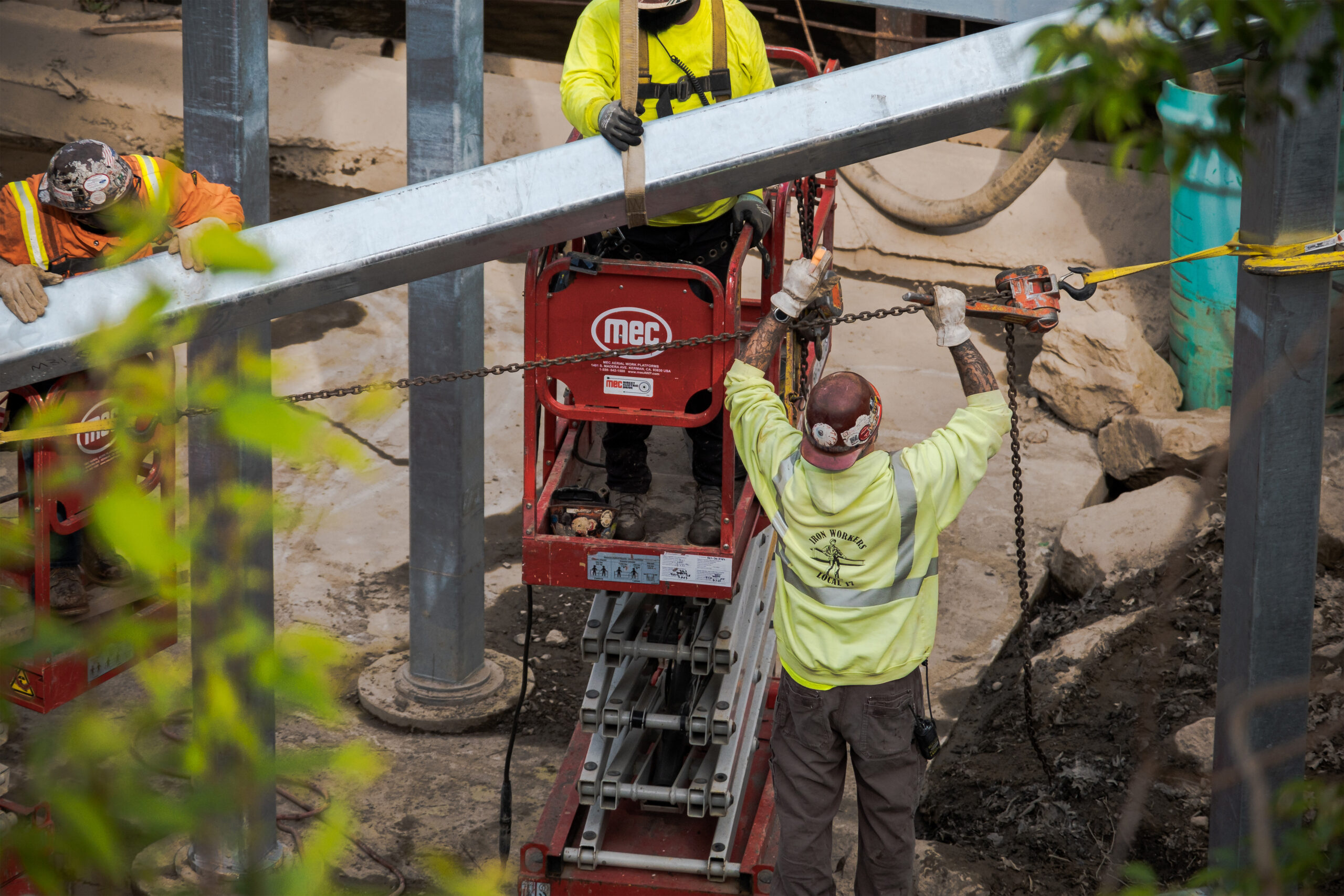 Two workers in safety vests operating red INGC lifting equipment to position steel beam outdoors