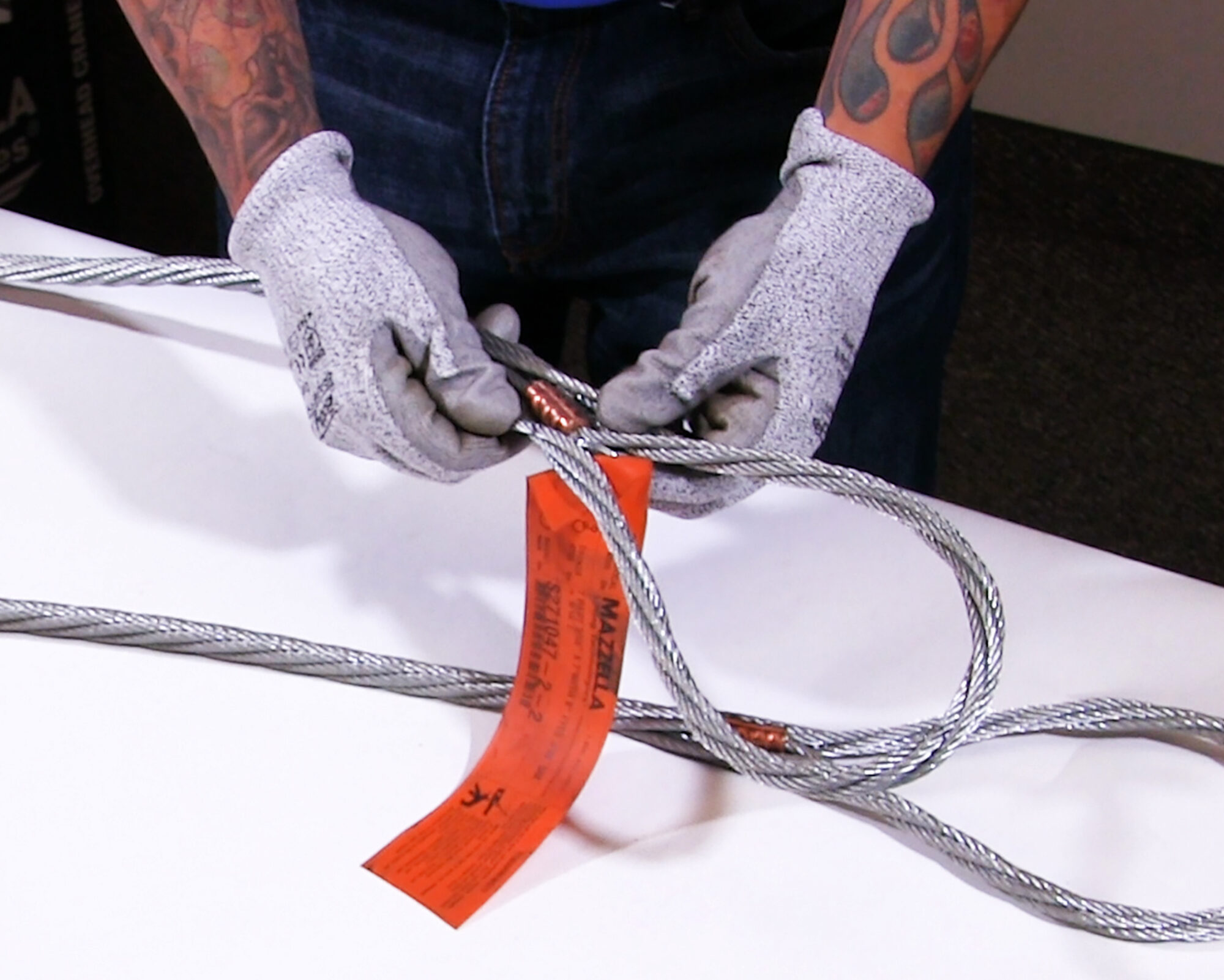 A multi-part wire rope sling with an orange Mazzella tag being inspected by a man wearing gloves.