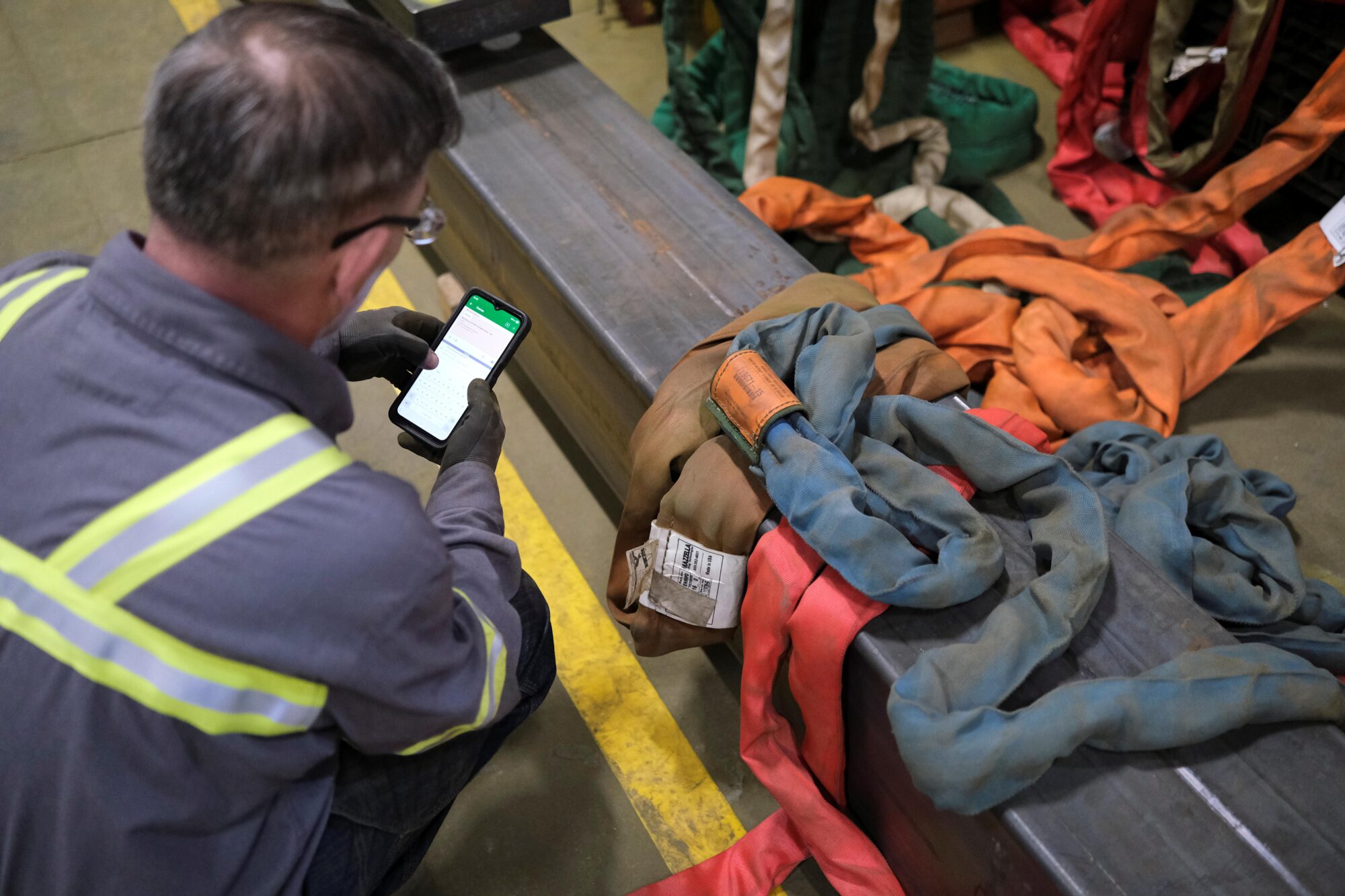 An inspector looking at his phone as he stands over a pile of used synthetic slings.